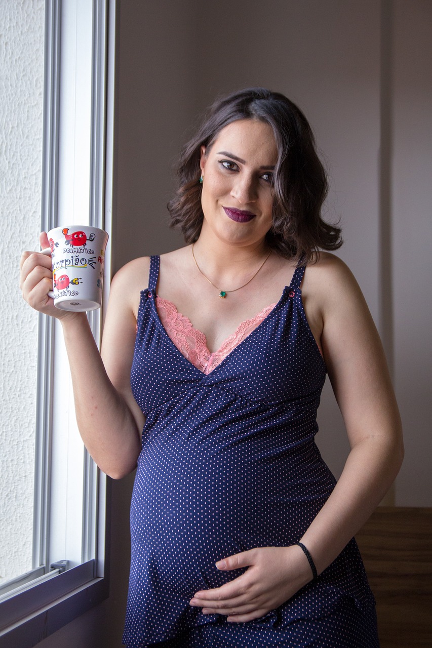 Pregnant woman is holding a mug with her vitamins inside of it
